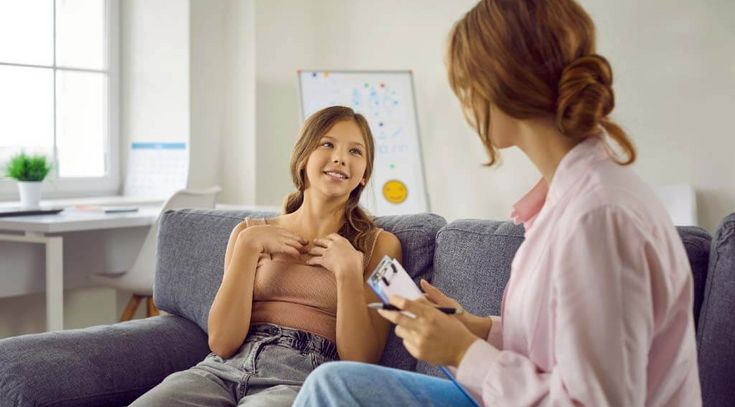 Teenagermädchen im Gespräch mit ihrer Mutter, auf dem Sofa sitzend