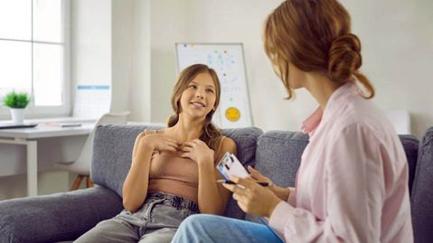 Teenagermädchen im Gespräch mit ihrer Mutter, auf dem Sofa sitzend