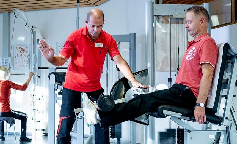 Männliche Person beim Krafttraining in der Reha, Therapeut unterstützt