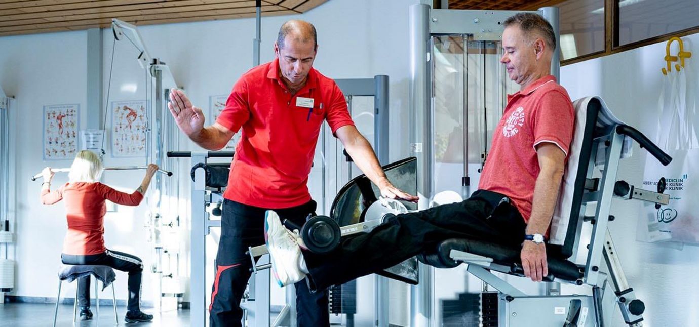Männliche Person beim Krafttraining in der Reha, Therapeut unterstützt