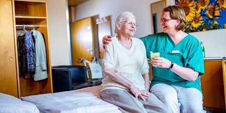 Fröhliche Plegerin gibt zufriedener Seniorin etwas zu trinken