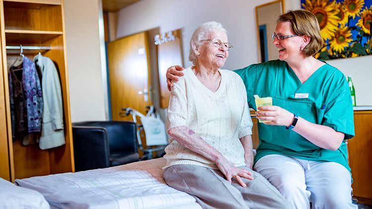 Fröhliche Plegerin gibt zufriedener Seniorin etwas zu trinken