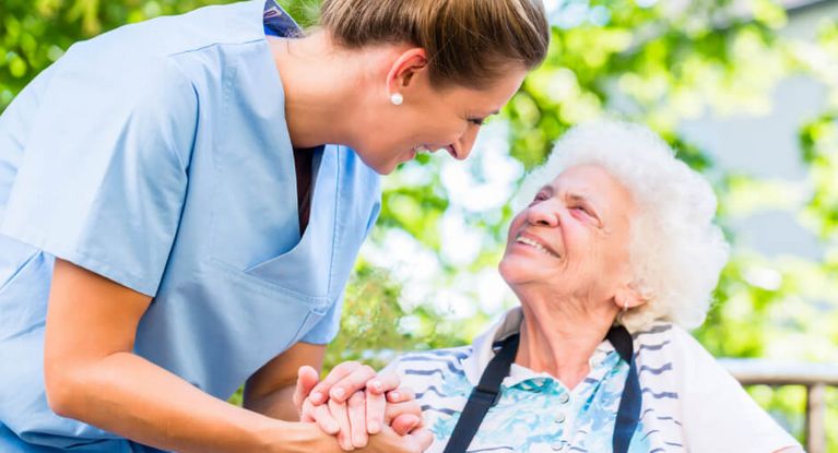 Altenpflegerin hält die Hand einer lächelnden Seniorin im Rollstuhl