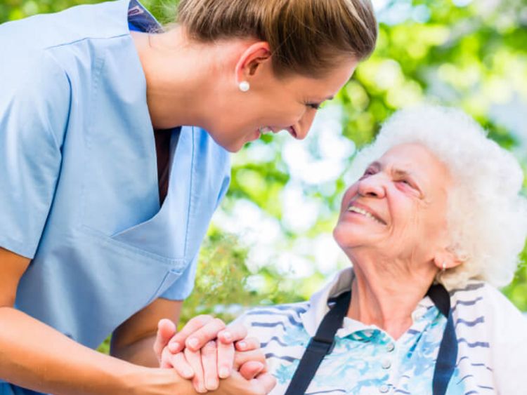 Altenpflegerin hält die Hand einer lächelnden Seniorin im Rollstuhl