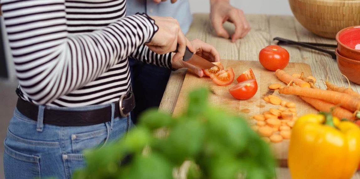 Eine weibliche Person schneidet Tomaten, weiteres Gemüse liegt daneben
