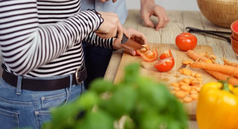 Eine weibliche Person schneidet Tomaten, weiteres Gemüse liegt daneben