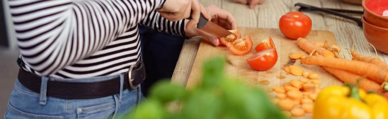 Eine weibliche Person schneidet Tomaten, weiteres Gemüse liegt daneben