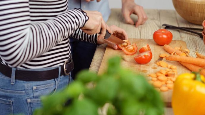 Eine weibliche Person schneidet Tomaten, weiteres Gemüse liegt daneben