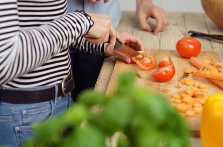 Eine weibliche Person schneidet Tomaten, weiteres Gemüse liegt daneben