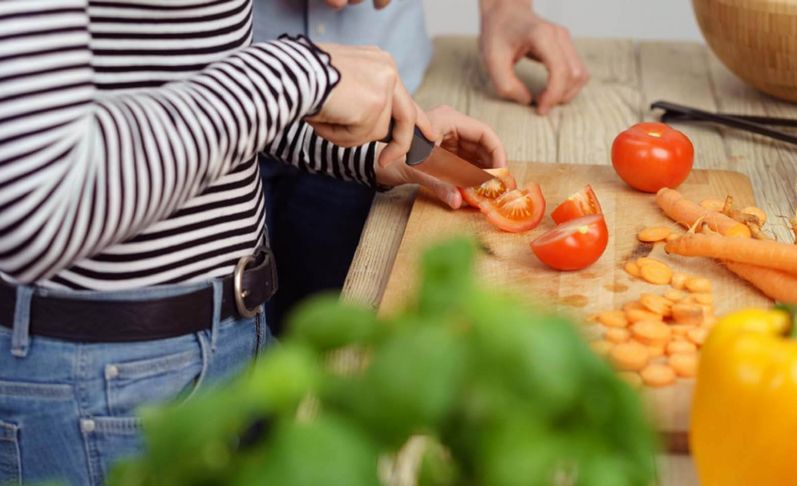 Eine weibliche Person schneidet Tomaten, weiteres Gemüse liegt daneben