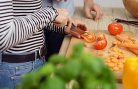 Eine weibliche Person schneidet Tomaten, weiteres Gemüse liegt daneben