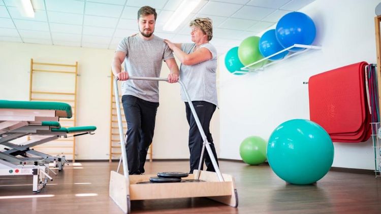 Patient beim Gehtraining in der Reha, Therapeutin unterstützt
