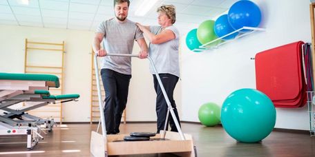 Patient beim Gehtraining in der Reha, Therapeutin unterstützt
